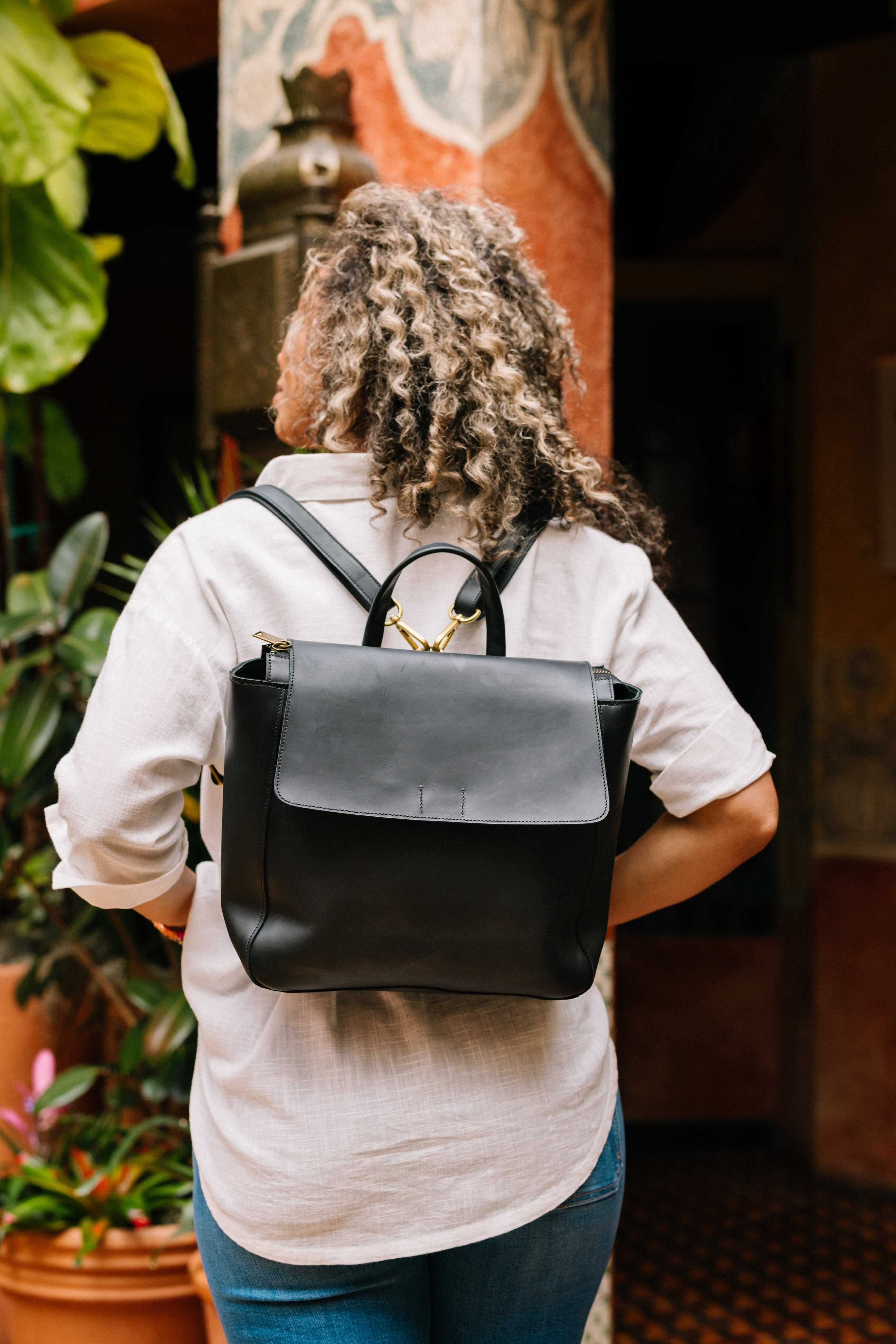 The interior back wall of the Debut Backpack is shown. The bag has a pink fabric lining with a white floral print. There is an interior zipper pocket stitched into the back wall. There is also a larger slot pocket along the back wall with a snap closure to keep it secure.