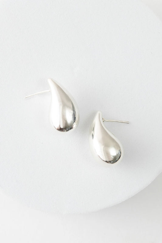 The Dew Drop Studs are mid-sized teardrop studs composed of shiny silver. The teardrop curves slightly, giving the earrings a more natural look.