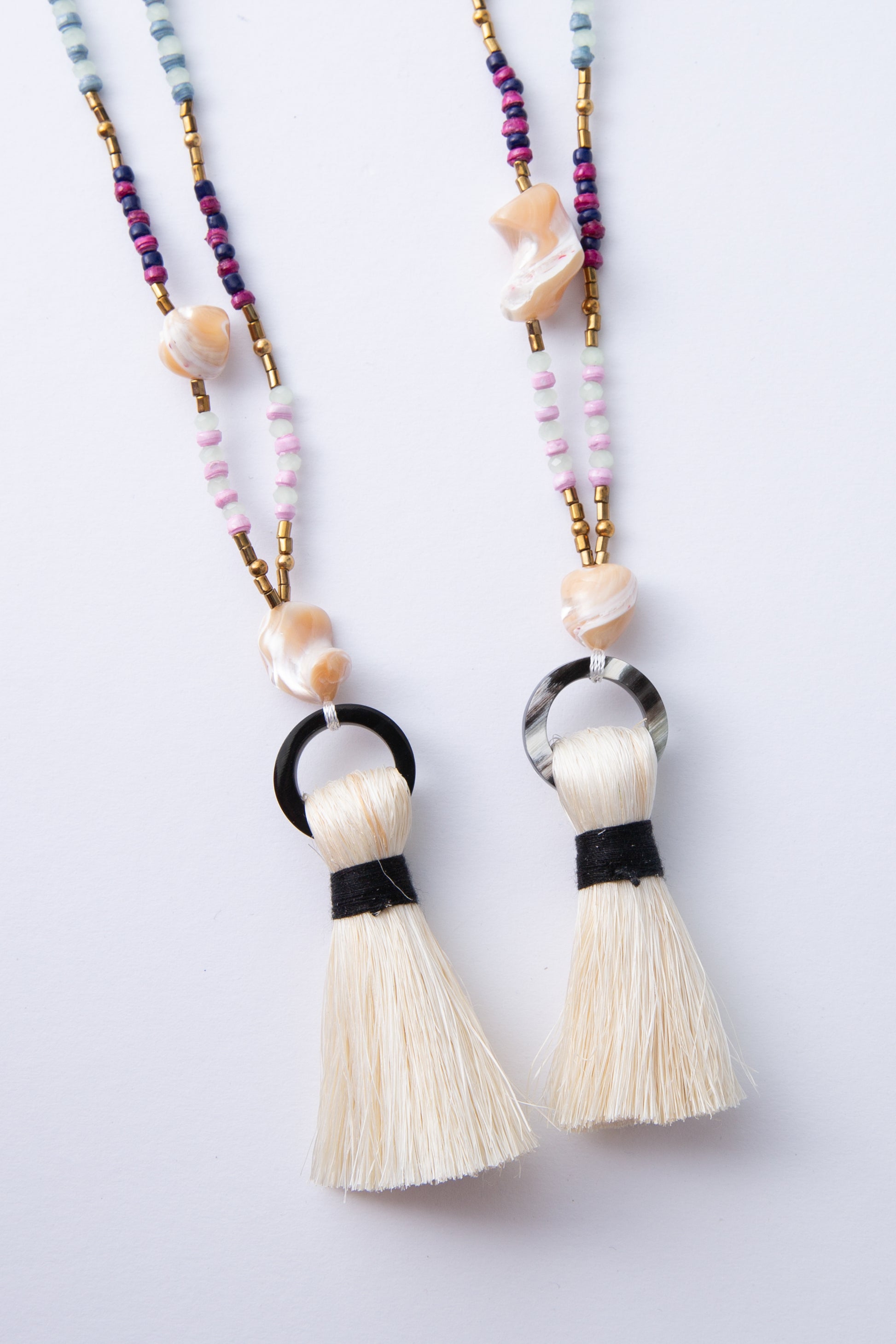 Two Dorah Necklaces are shown side by side. The horn circle at the bottom of each necklace varies in shade due to the natural material used to craft it. One is solid black, while the other is black with white streaks.