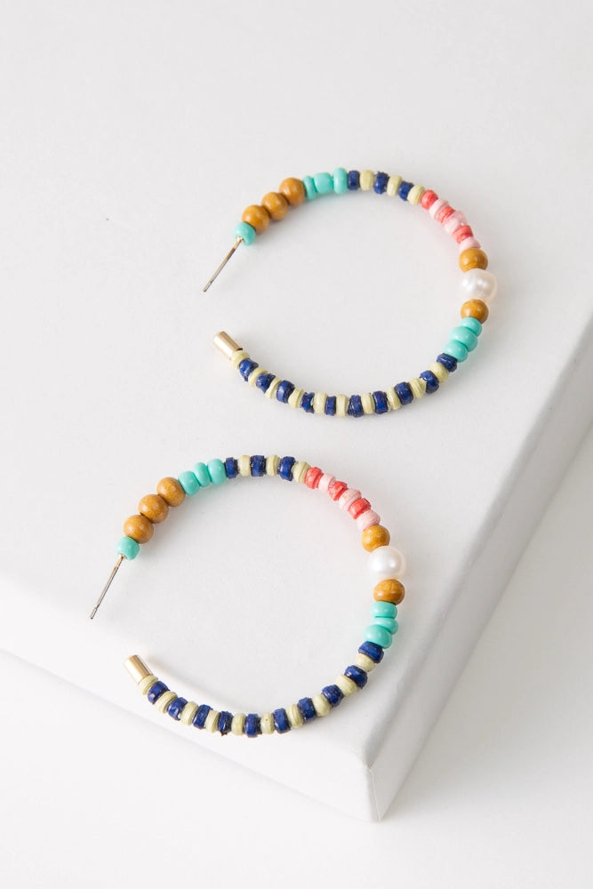 The Harbor Hoops are large hoop earrings strung with a variety of beads. The beads include tiny handrolled paper beads in shades of blue, cream, pink, and dark pink. Sections of paper beads alternate with wooden, pearl, and turquoise glass beads.