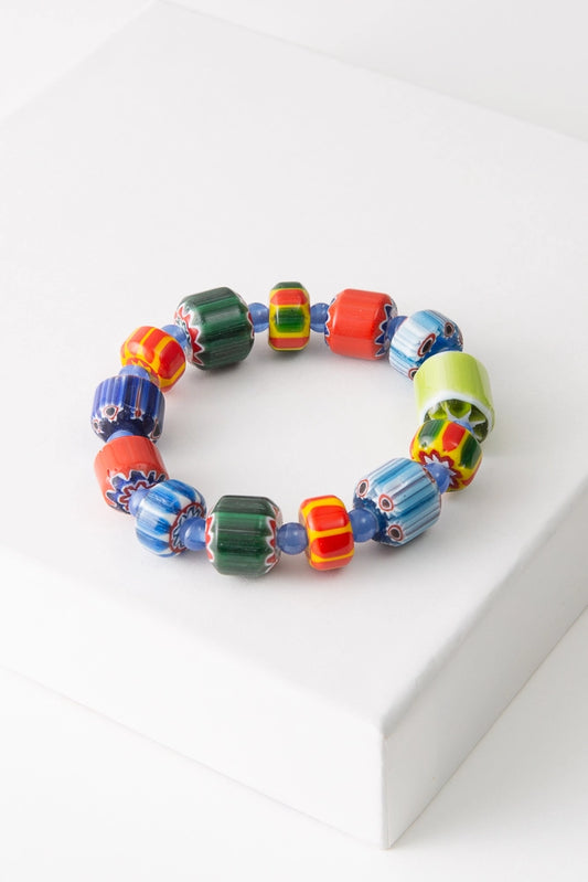 The Lampwork Glass Bead Bracelet is a single strand bracelet composed of handcrafted lampwork beads. The beads include different floral and striped patterns crafted into the glass in shades of green, orange, yellow, and blue. Small spherical blue glass beads are placed between the lampwork beads.