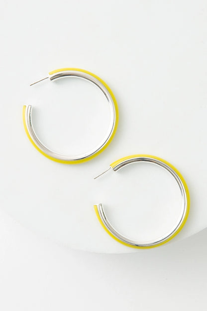 The Lima Hoops are large hoop earrings that are open at the back. The interior of the hoop is shining silver metal, and the exterior of the hoop is bright yellow resin.