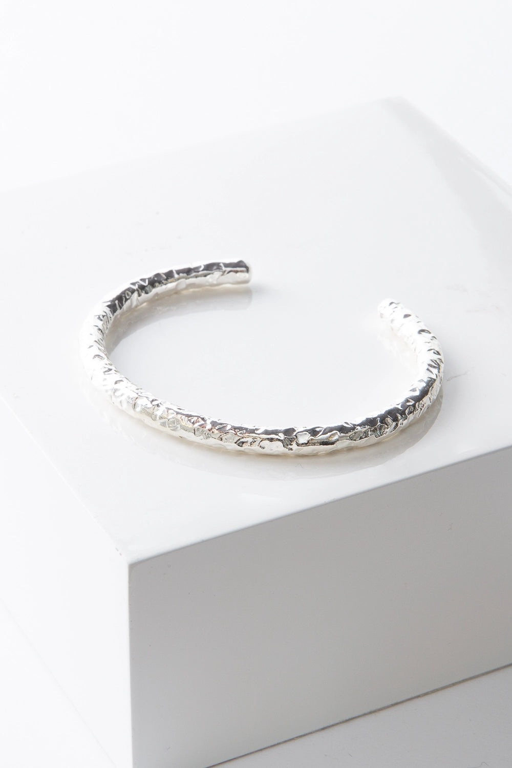 The Molten Metal Cuff is a skinny silver plated bronze cuff that is open at the back, allowing it to be slid onto the wrist. The shiny silver metal has a rounded shape and an irregular hammered texture.
