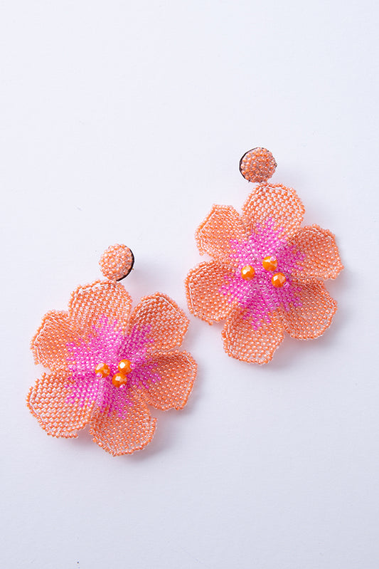 The New Bloom Earrings are composed of tiny peach and pink glass beads crafted in the shape of a large flower. Larger peach beads are stitched onto the center of the blooms. The flowers hang down from posts that are covered in tiny peach beads. 