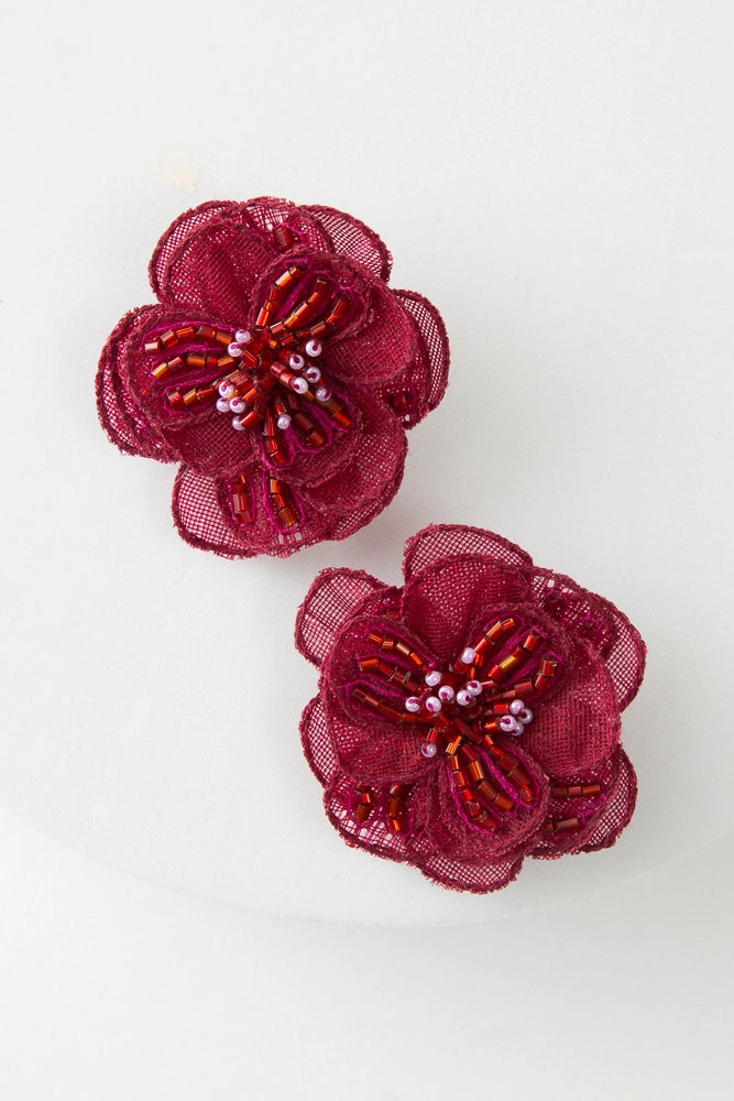 The Organza Earrings are large stud-style earrings composed of layers of crimson organza fabric petals that form a flower. In the middle of the flower are white and red glass beads that form the flower's center.