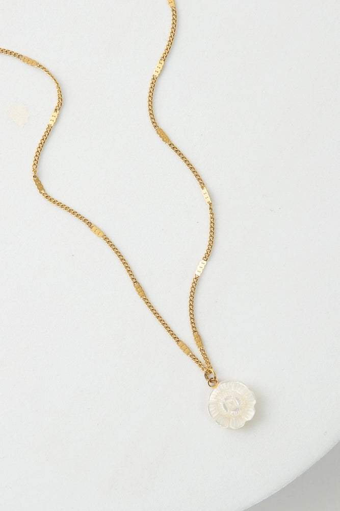 The Petite Bloom Necklace has a dainty gold chain with a small white flower pendant. The flower is composed of shining mother-of-pearl.