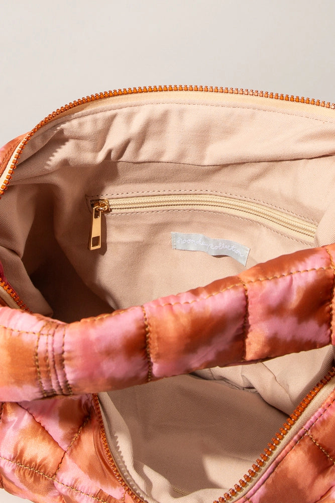 The Quilted Zipper Tote is shown unzipped, revealing the interior, which is lined in cream colored fabric. There is a zipper pocket stitched into the back wall of the bag.