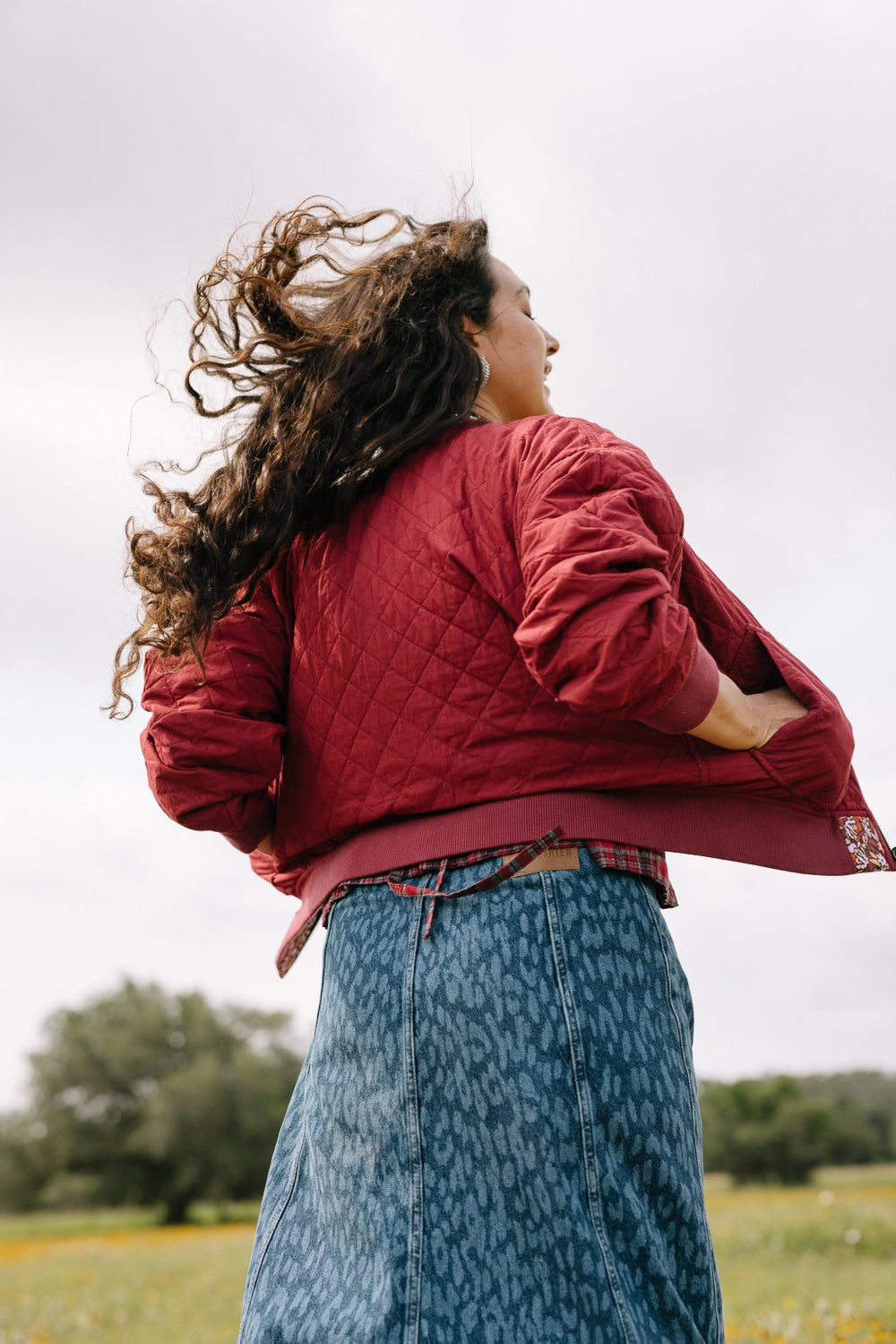 The bomber jacket is shown worn with its floral print on the interior of the jacket. The exterior is a solid burgundy cotton fabric with a quilted texture.