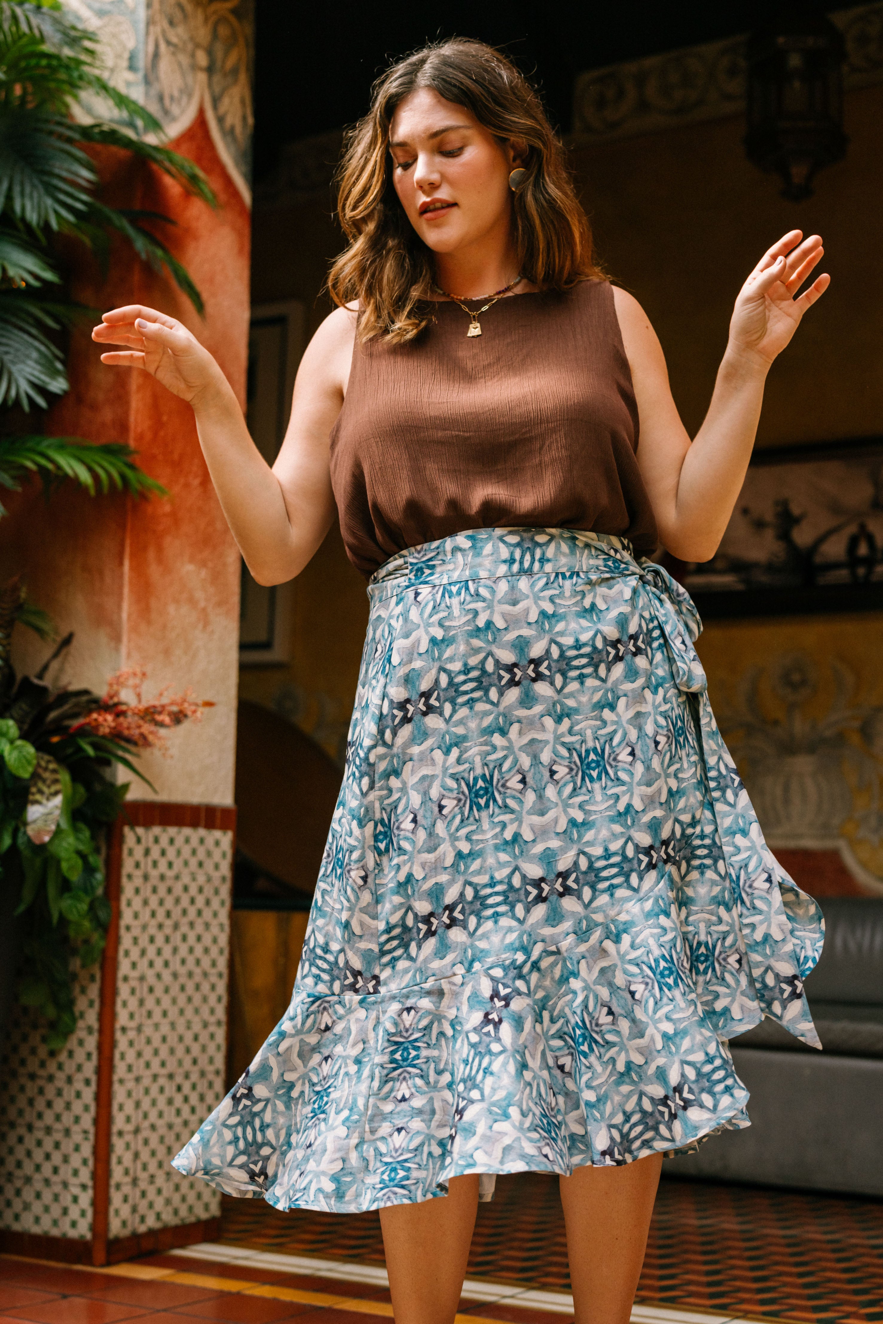 The Ruffle Skirt is a flowy skirt that hits mid-calf. It is a wrap skirt made out of blue and white fabric with a geometric, mediterannean-inspired print. The skirt wraps around and is fastened at the hip with a fabric tie in the same fabric as the skirt. The skirt has a slight ruffled effect at the bottom. 
