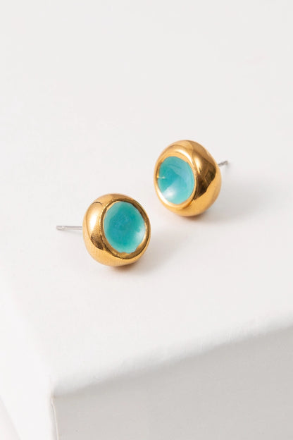 The Sculpted Porcelain Studs are composed of turquoise porcelain shaped into a small circle that is concave in the center. Shining gold luster coats the exterior rim of the studs, serving as a border.