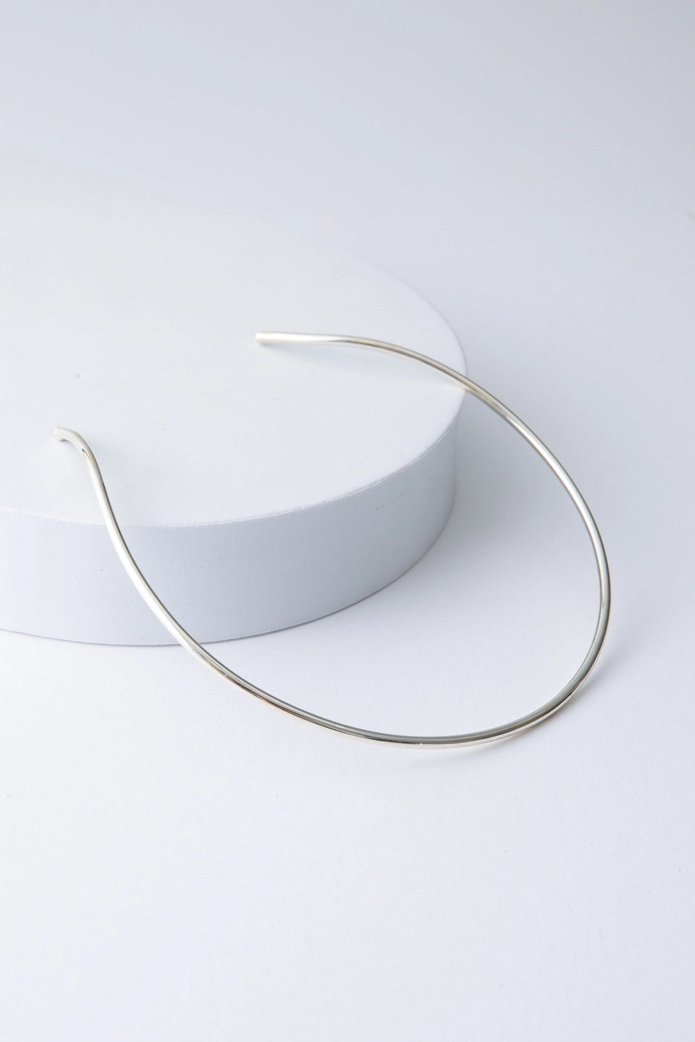 This is a choker-style necklace composed of a single bar of shiny silver plated bronze that forms a semi-circle. It is open in the back, allowing it to be slid onto the neck. 