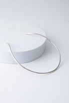 This is a choker-style necklace composed of a single bar of shiny silver plated bronze that forms a semi-circle. It is open in the back, allowing it to be slid onto the neck. 