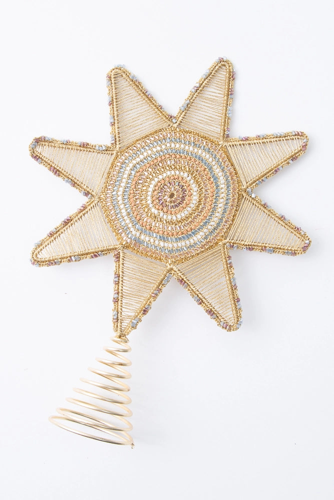 The Starlight Beaded Tree Topper has a gold coil base where the topper can be slid onto the tree. On top of the base is a large, eight-pointed star. The outline of the star is gold metal with silver and gold glass beads stitched to it. The points of the star are filled with many rows of metallic gold thread. The center of the star is composed of many concentric circles of glass beads in shades of gold, white, and silver.