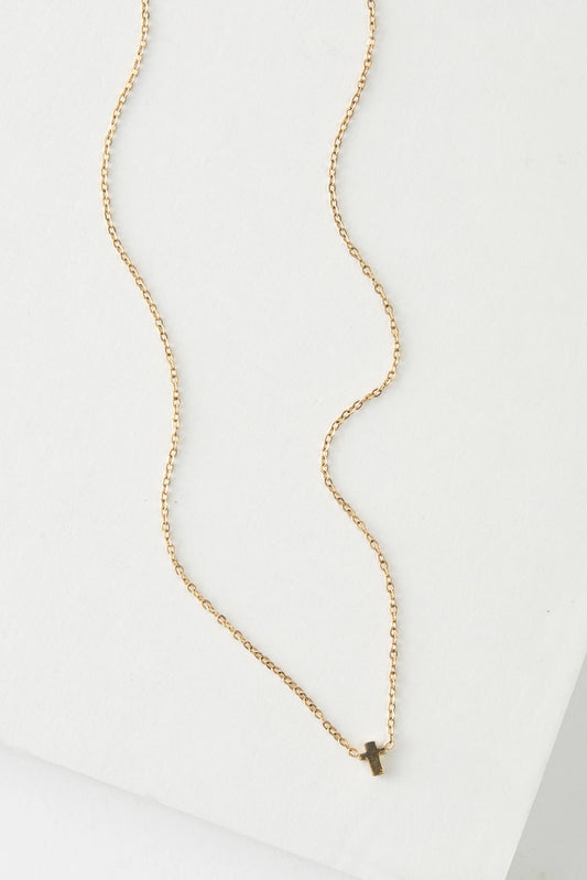 The Steadfast Necklace in gold is a dainty gold chain necklace. At the bottom is a tiny gold cross charm.