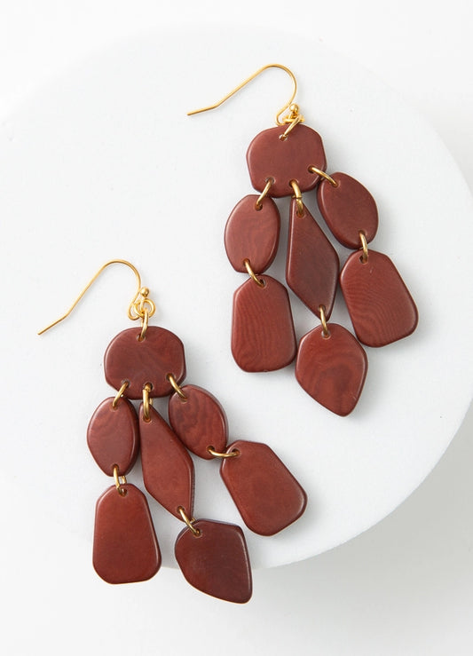 The Tagua Cascada Earrings are chandelier-style earrings with gold ear hooks. They are composed of polished pieces of tagua seed that have been cut into geometric shapes. The tagua is a rich rust shade. Each piece is linked with a gold jump ring to form a chandelier look.