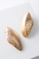 These are post-style earrings composed of shining gold-plated brass with a hammered texture. The earrings have an irregular, organic look and are roughly diamond shaped, with smooth rounded edges.