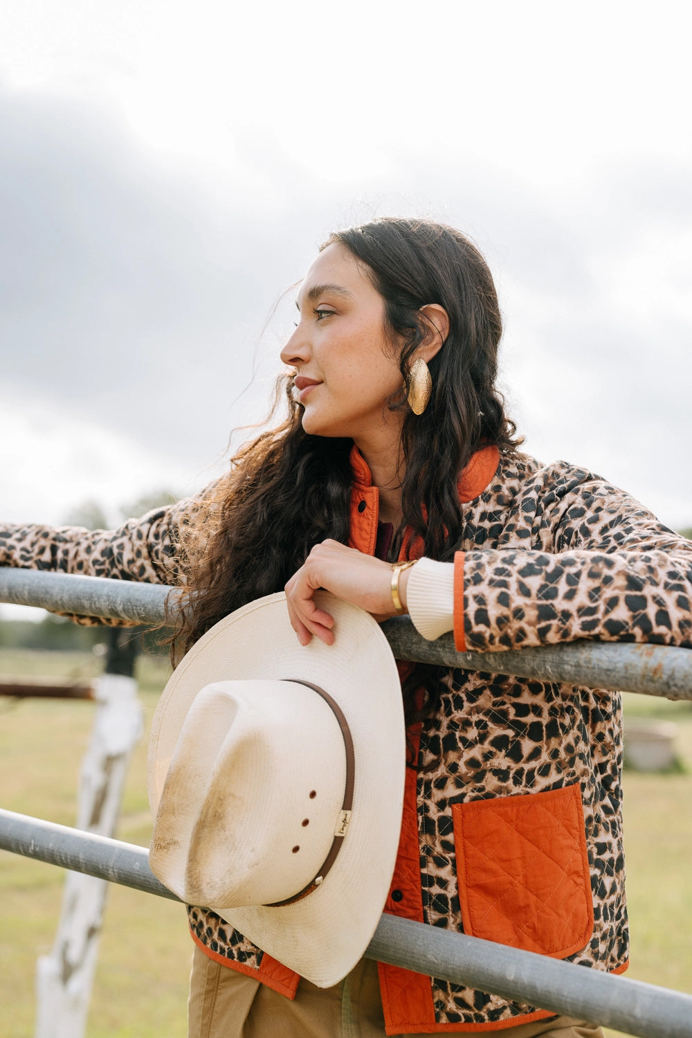 This jacket has a quilted texture and is composed of 100% cotton. The bulk of the jacket is leopard print fabric, and the collar, cuffs, button closure, and pockets are bright orange fabric. There are two large pockets that are open at the top. The jacket has black snap buttons along the front as a closure.