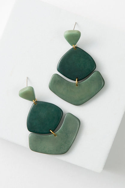 The Tortuga Earrings are composed of polished tagua seed in different shades of jade green. At the top of the earrings is a post with a triangular piece of tagua attached to it. Geometric pieces of tagua hang down below the post.