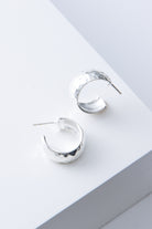 These are chunky, demi-hoop earrings that are open at the back. They are composed of flattened silver plated bronze with a hammered texture. The hoops are attached to a steel post.