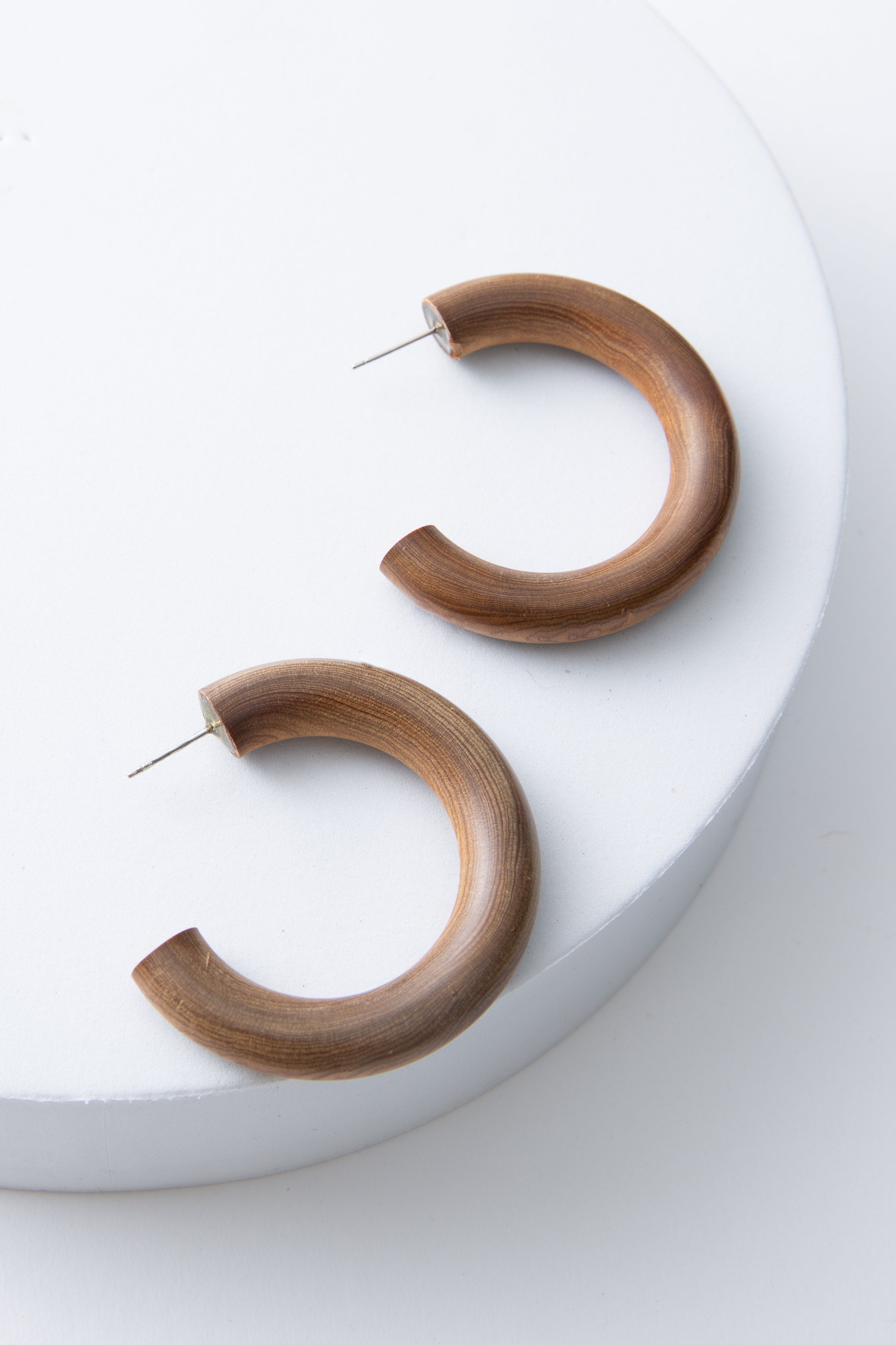 These are demi-hoops that are open at the back. They are composed entirely of a round, smooth piece of natural brown wood that curves around to form the hoop. The earrings have steel ear posts. 